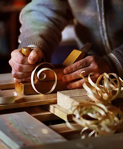 Mains d’artisan rabotant une pièce de bois, copeaux en premier plan
